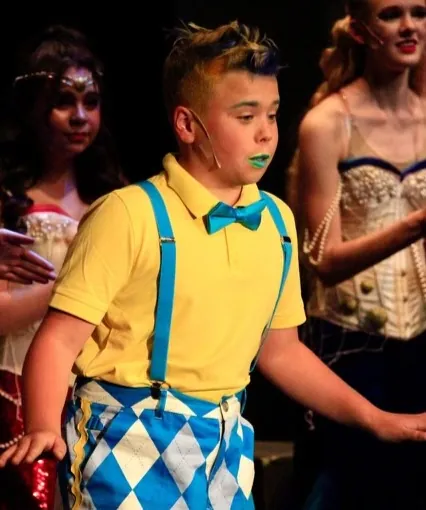 A young performer in a yellow shirt and bow tie singing on stage in Seussical Jr.